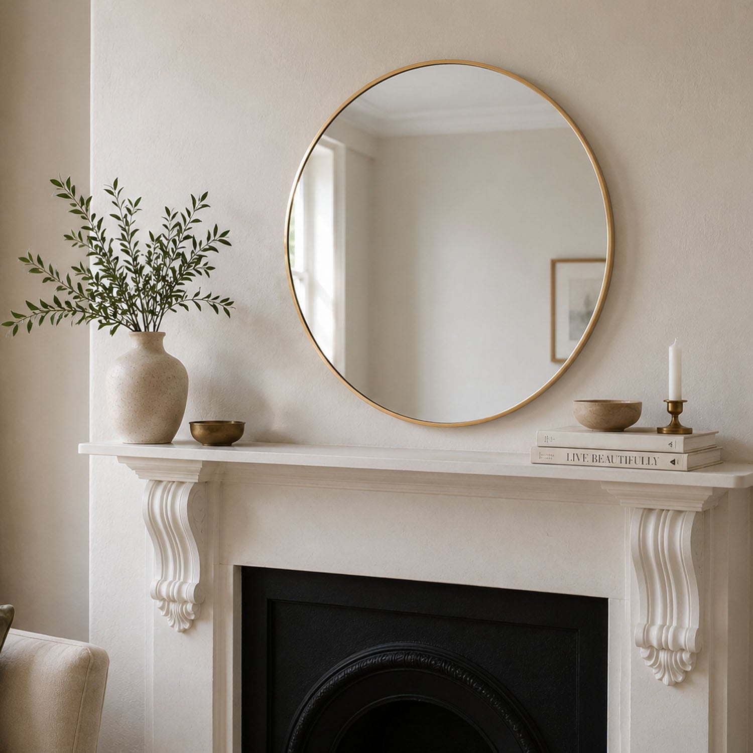 Round gold aluminium mirror styled above a fireplace mantel in a neutral living room.