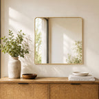 Gold aluminium mantel mirror styled above a wooden console table with decorative vases and books in a warm neutral room.