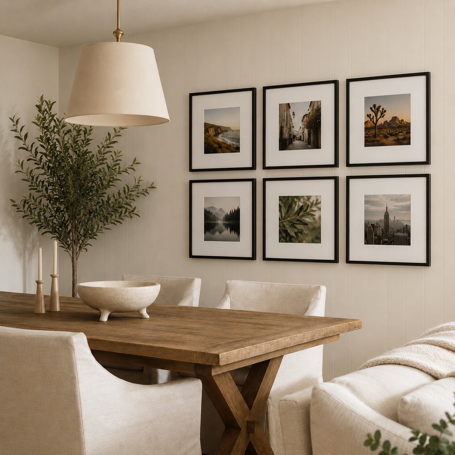 A warm, contemporary dining room features a wooden table, upholstered chairs, and a gallery wall of six black-framed photographs arranged in a neat grid beneath a large pendant light.