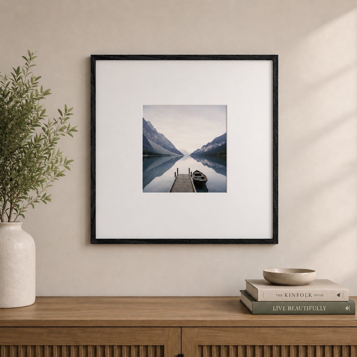 A black woodgrain square photo frame with a white mat showcases a tranquil lakeside landscape and is styled above a wooden console with neutral décor in a contemporary interior.