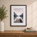 A black wood-look photo frame with a wide white mat beautifully showcases a tranquil lakeside landscape, styled above a timber sideboard in a warm, contemporary interior.