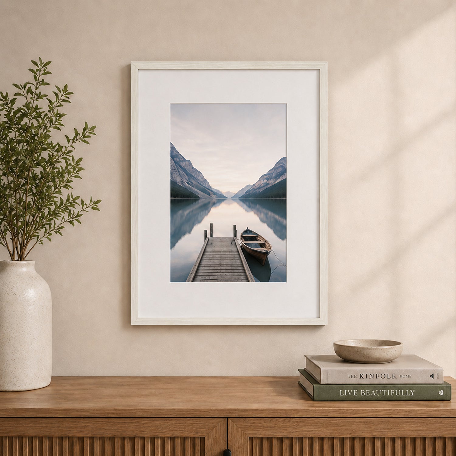 A white wood-look photo frame with a wide white mat beautifully showcases a tranquil lakeside landscape, styled above a timber sideboard in a warm, contemporary interior.