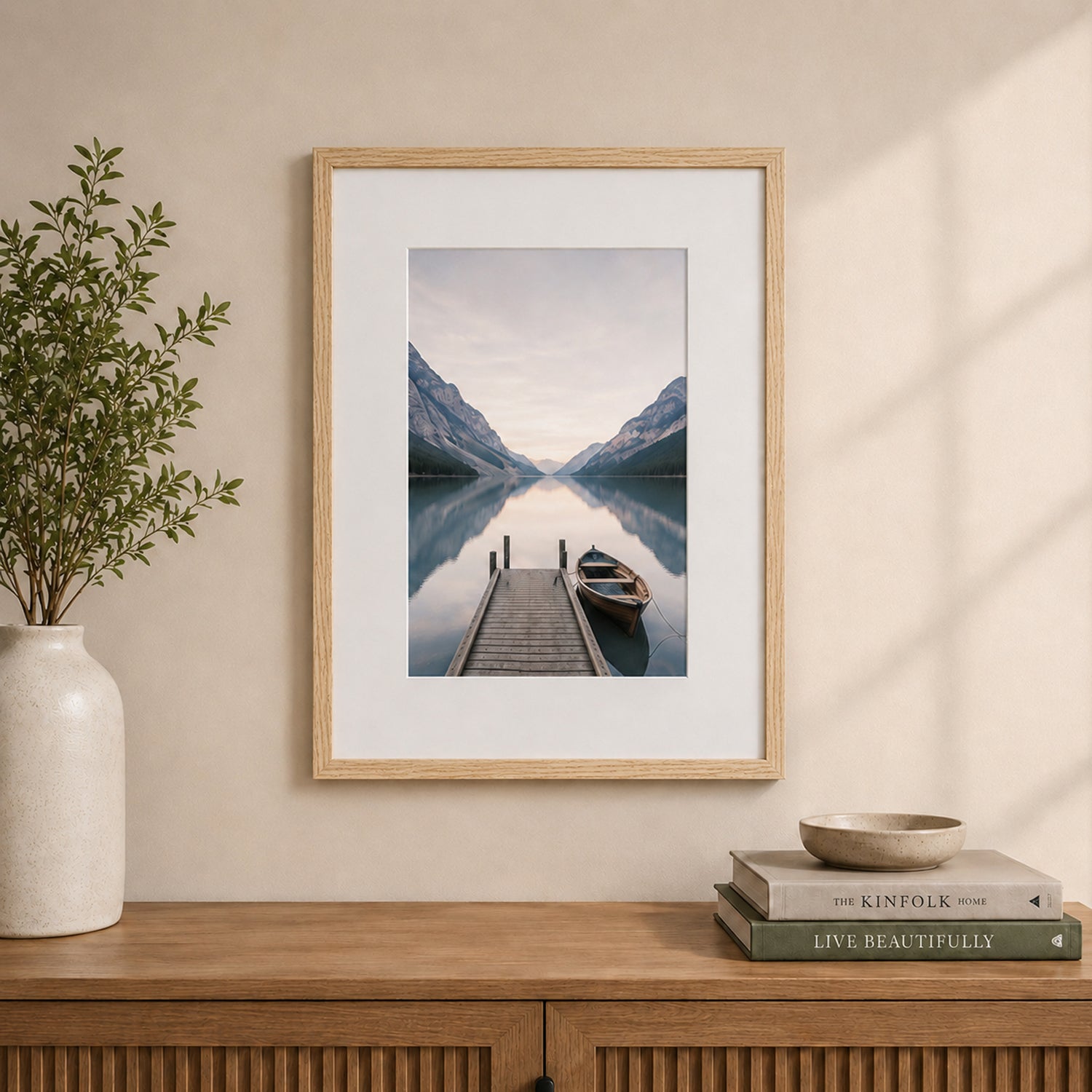 A natural wood-look photo frame with a wide white mat beautifully showcases a tranquil lakeside landscape, styled above a timber sideboard in a warm, contemporary interior.