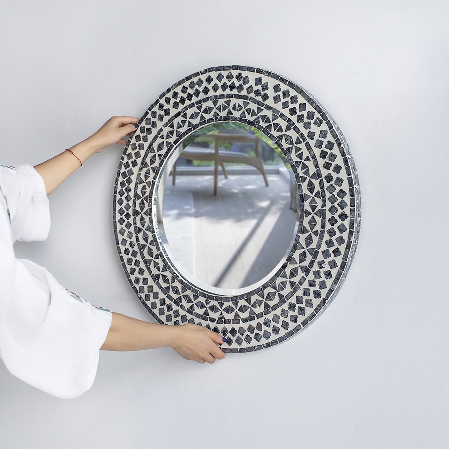 Design Republique Algaia round wall mirror shown being positioned on a wall, highlighting the detailed grey and white patterned frame.