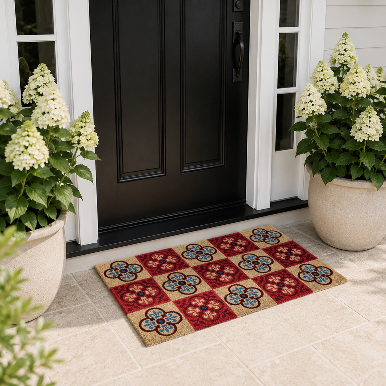 A colourful checkered coir doormat with bold floral tile motifs adds vibrant character and a welcoming touch to this elegant modern entryway, framed by lush white hydrangeas and a black front door.
