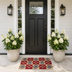 A colourful checkered coir doormat with bold floral tile motifs adds vibrant character and a welcoming touch to this elegant modern entryway, framed by lush white hydrangeas and a black front door.