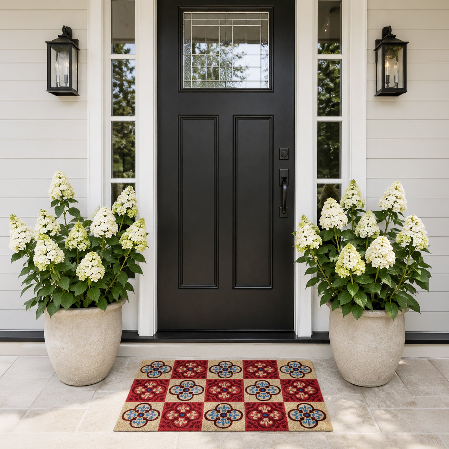A colourful checkered coir doormat with bold floral tile motifs adds vibrant character and a welcoming touch to this elegant modern entryway, framed by lush white hydrangeas and a black front door.
