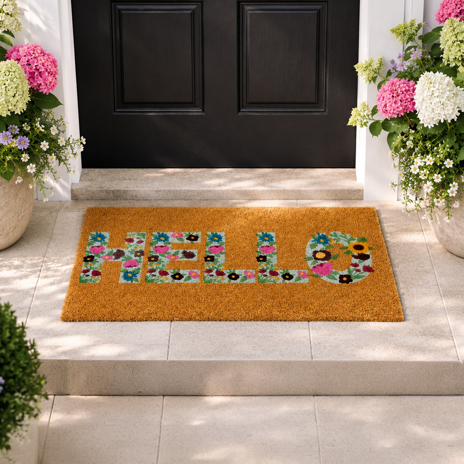 A cheerful "HELLO" coir doormat with colourful floral lettering creates a warm, inviting entrance, beautifully framed by blooming hydrangeas and a classic black front door.