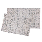 Two rectangular placemats with an all-over floral and leaf pattern in muted blue-gray and beige tones, shown overlapping on a plain white background.
