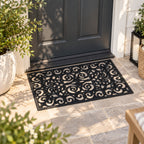 Design Republique Gabriel Rubber Mat in black, featuring decorative scrollwork, placed on a tiled outdoor entranceway in front of a black door.