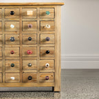 Close-up of a rustic wooden multi-drawer cabinet showcasing a variety of decorative drawer knobs in different colours, shapes and finishes.
