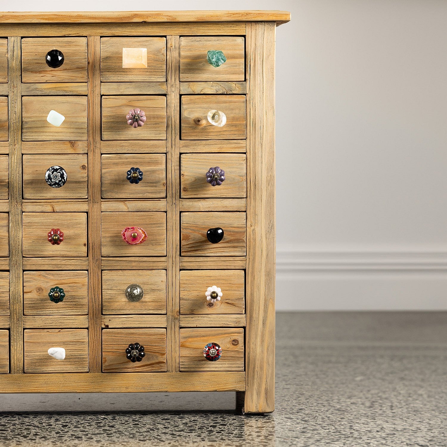 Close-up of a rustic wooden multi-drawer cabinet showcasing an assortment of decorative drawer knobs in different colours, shapes, materials and finishes.
