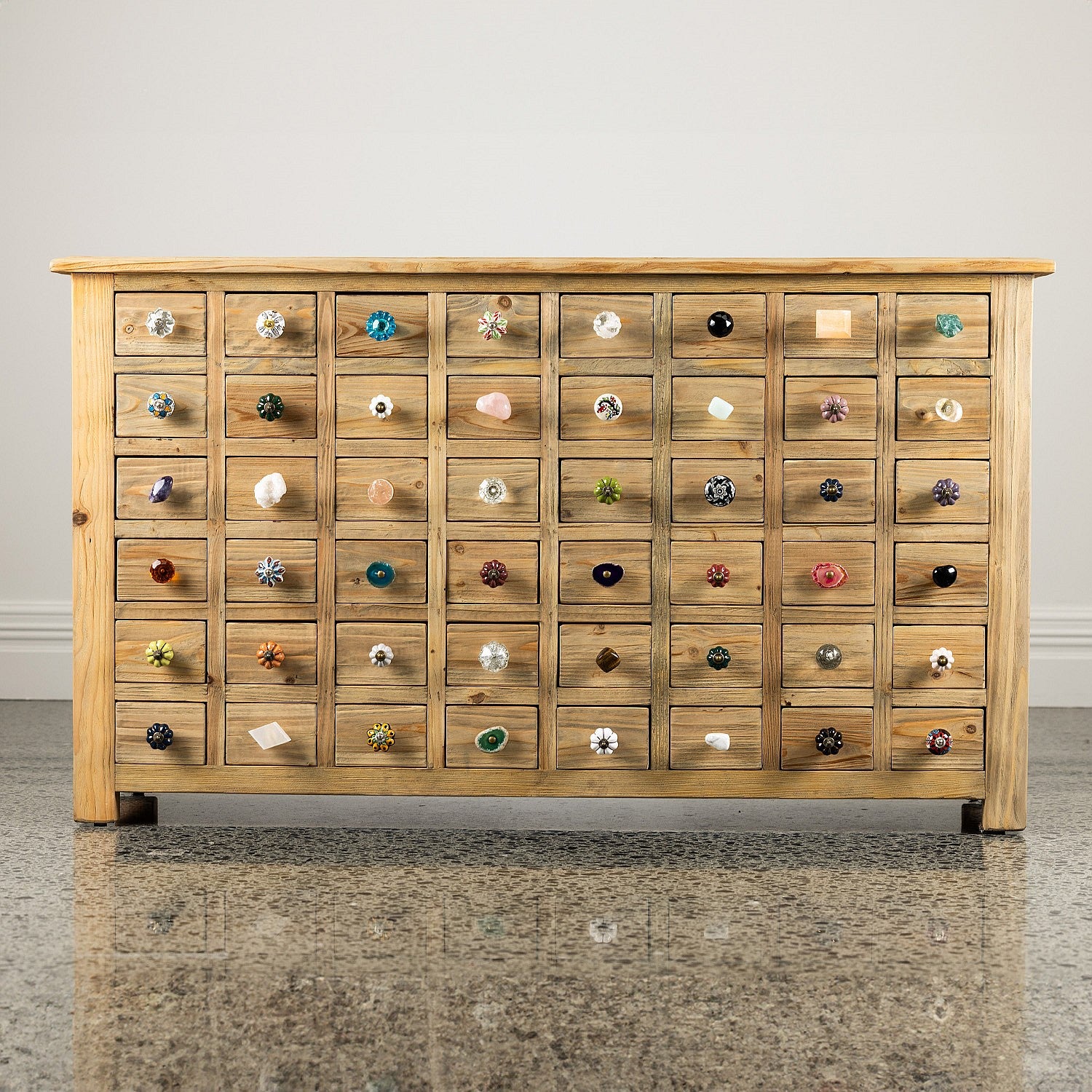 Rustic wooden apothecary-style cabinet featuring multiple small drawers, each finished with a unique decorative drawer knob in a variety of colours, materials and designs.
