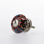 Round ceramic drawer knob with red, blue and black floral pattern detailing and silver metal centre accent.
