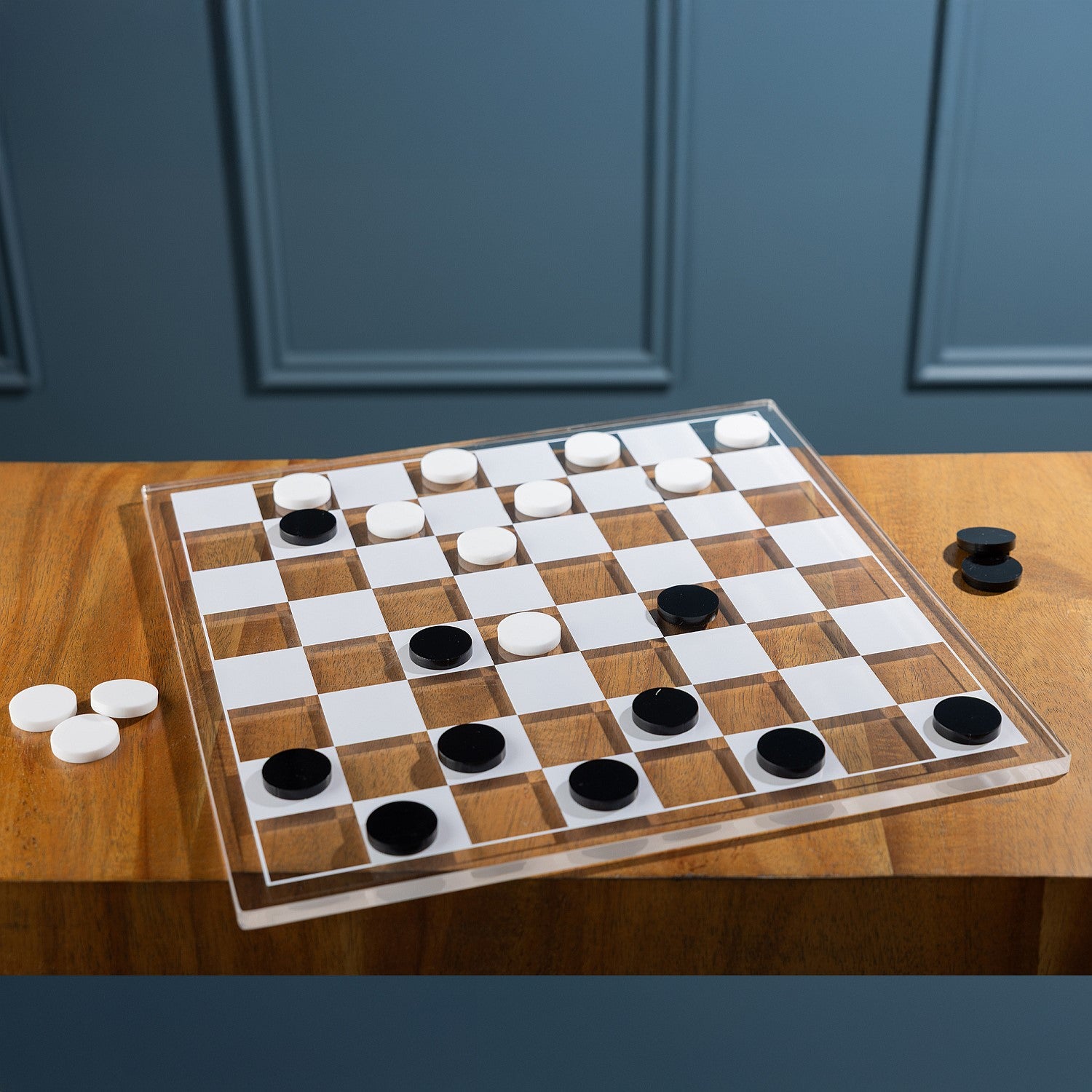Checkers game in progress featuring black and white playing pieces on a clear acrylic checkerboard 
