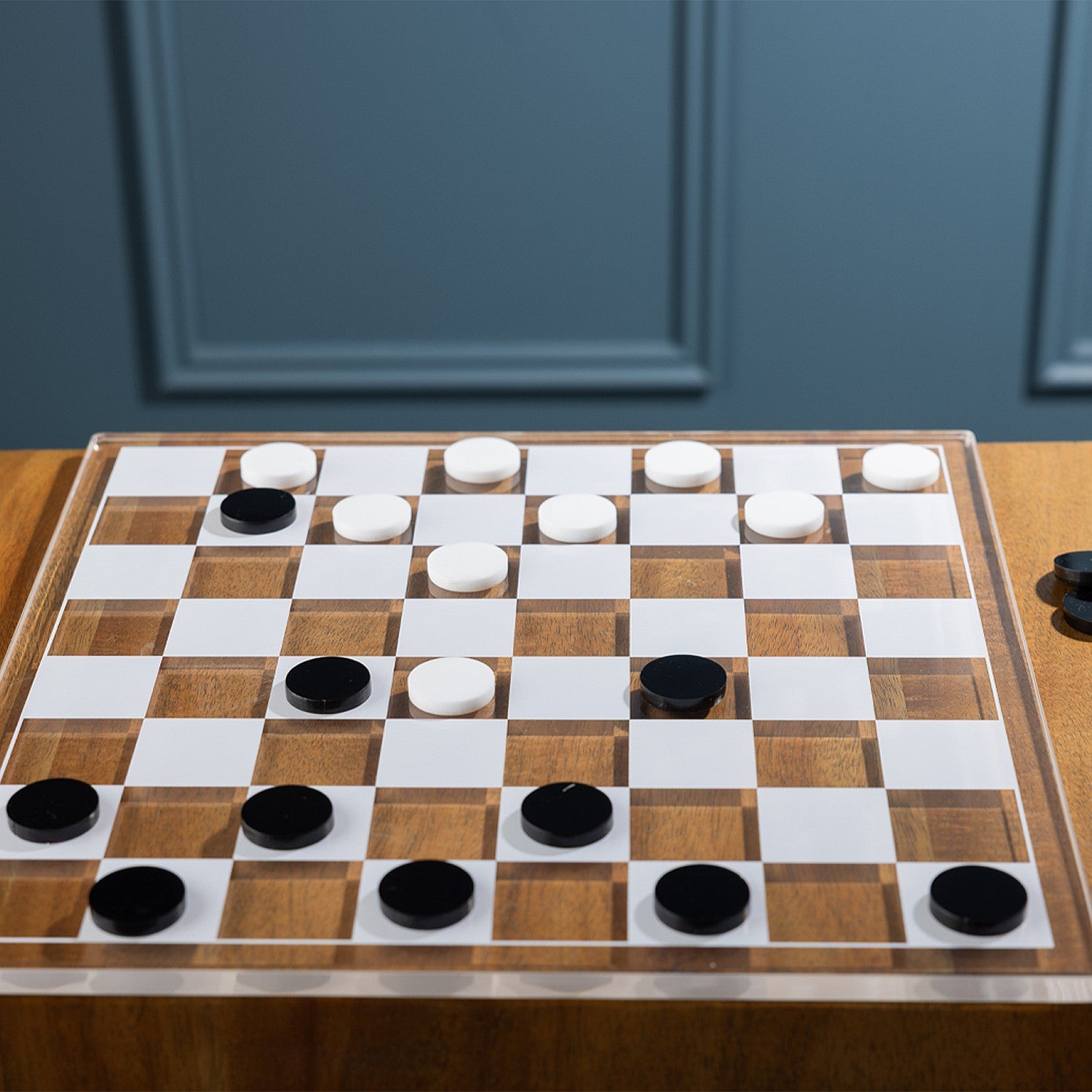 Checkers game in progress featuring black and white playing pieces on a clear acrylic checkerboard.

