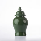 A glossy dark green ceramic lidded jar with a pointed lid finial, photographed against a clean white studio background.