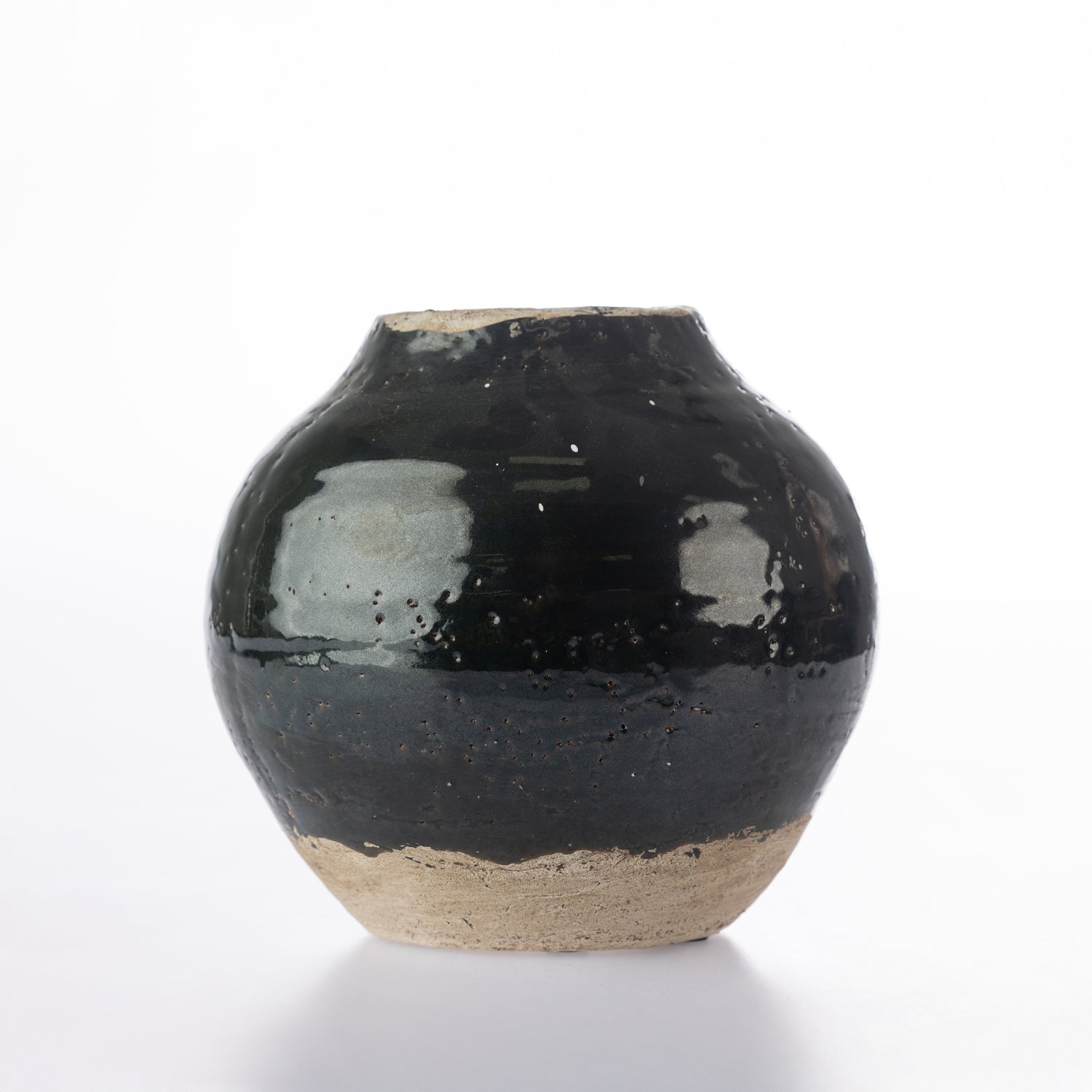A small round ceramic vase with a glossy black glaze and a natural beige clay foot, photographed on a clean white background.