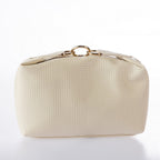 Cream textured cosmetic bag with gold ring hardware and zip closure on a white background.