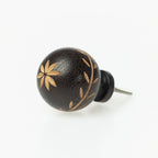 Dark wooden round drawer knob with engraved floral and leaf detailing and metal screw fitting.
