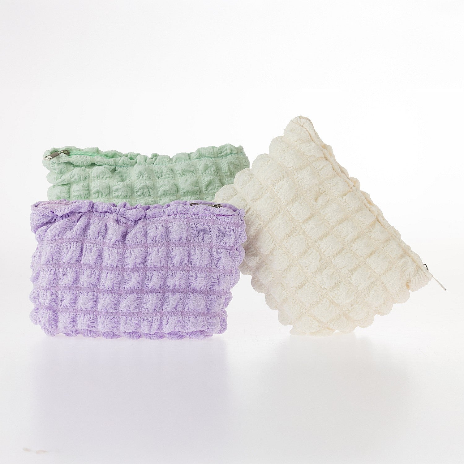 Textured waffle cosmetic pouches in mint, lilac, and cream displayed together on a white background.