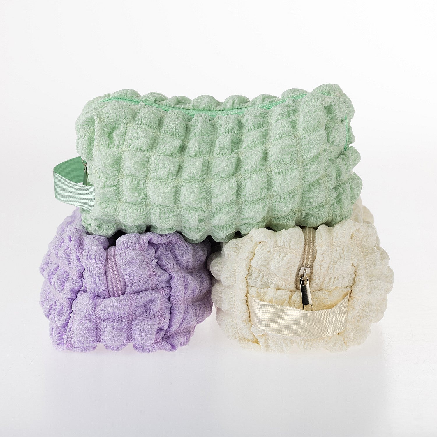 Group of textured waffle toiletry bags in green, lilac, and cream displayed on a white background.