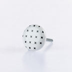 White ceramic round drawer knob with black star pattern detailing and metal screw fitting.
