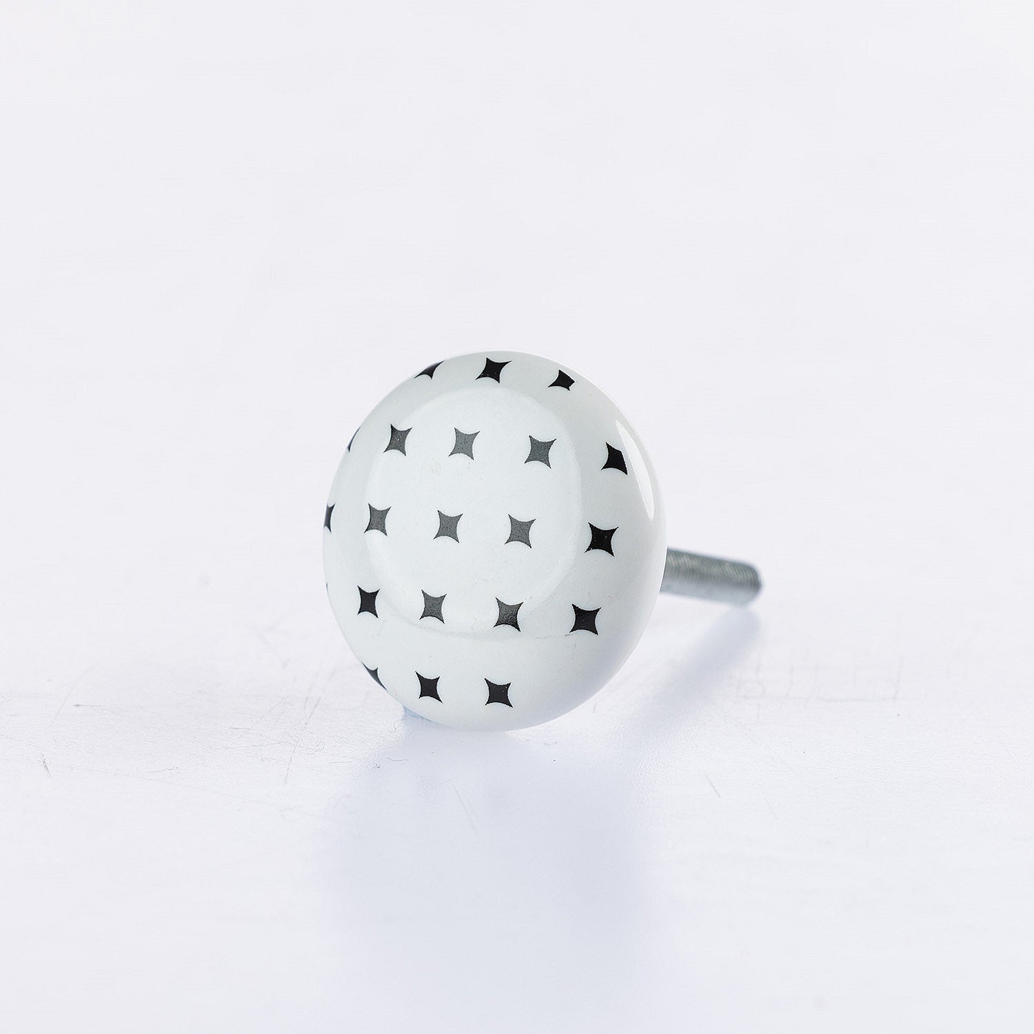 White ceramic round drawer knob with black star pattern detailing and metal screw fitting.
