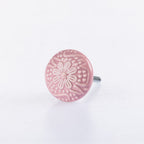 Pink ceramic round drawer knob with embossed floral pattern detailing and metal screw fitting.