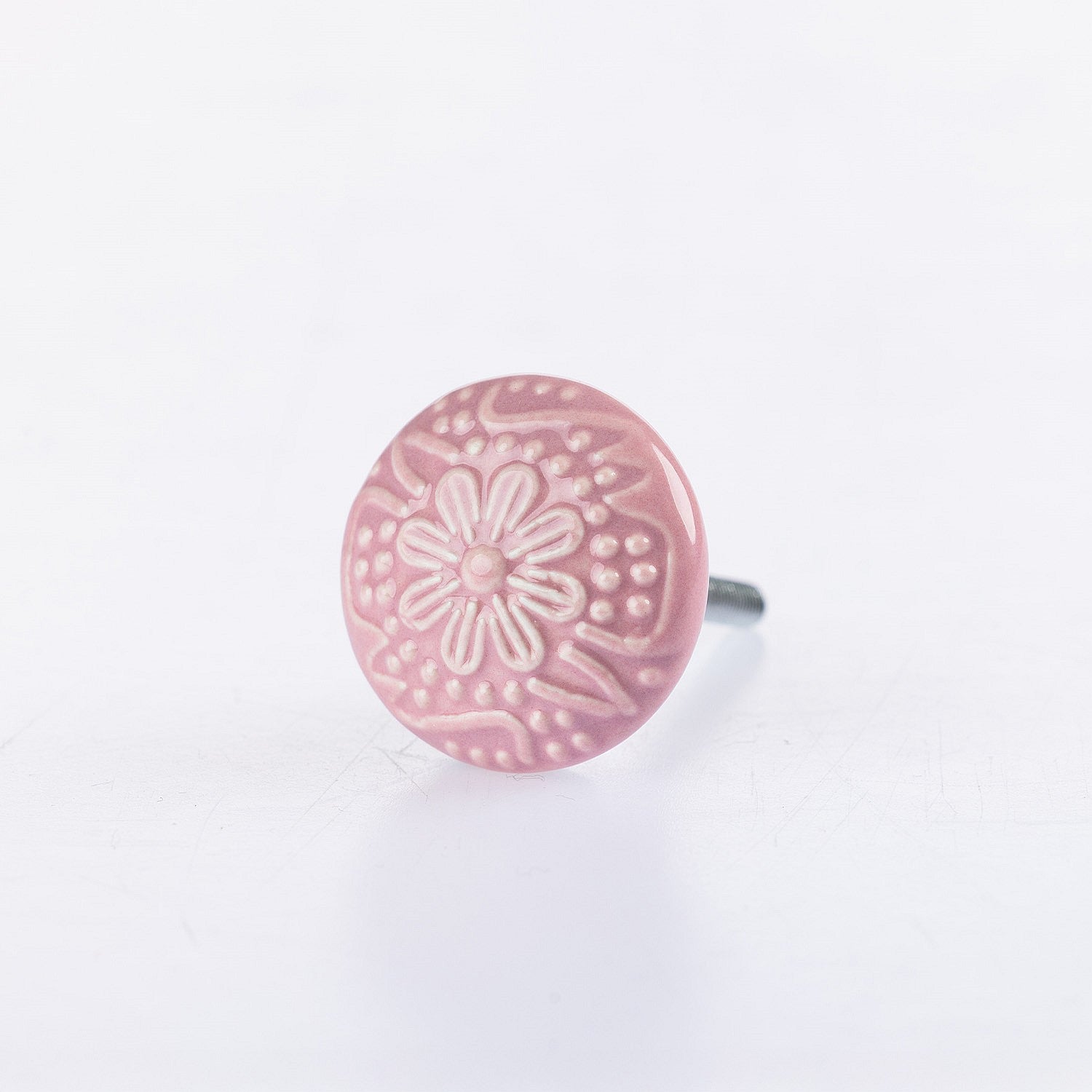Pink ceramic round drawer knob with embossed floral pattern detailing and metal screw fitting.
