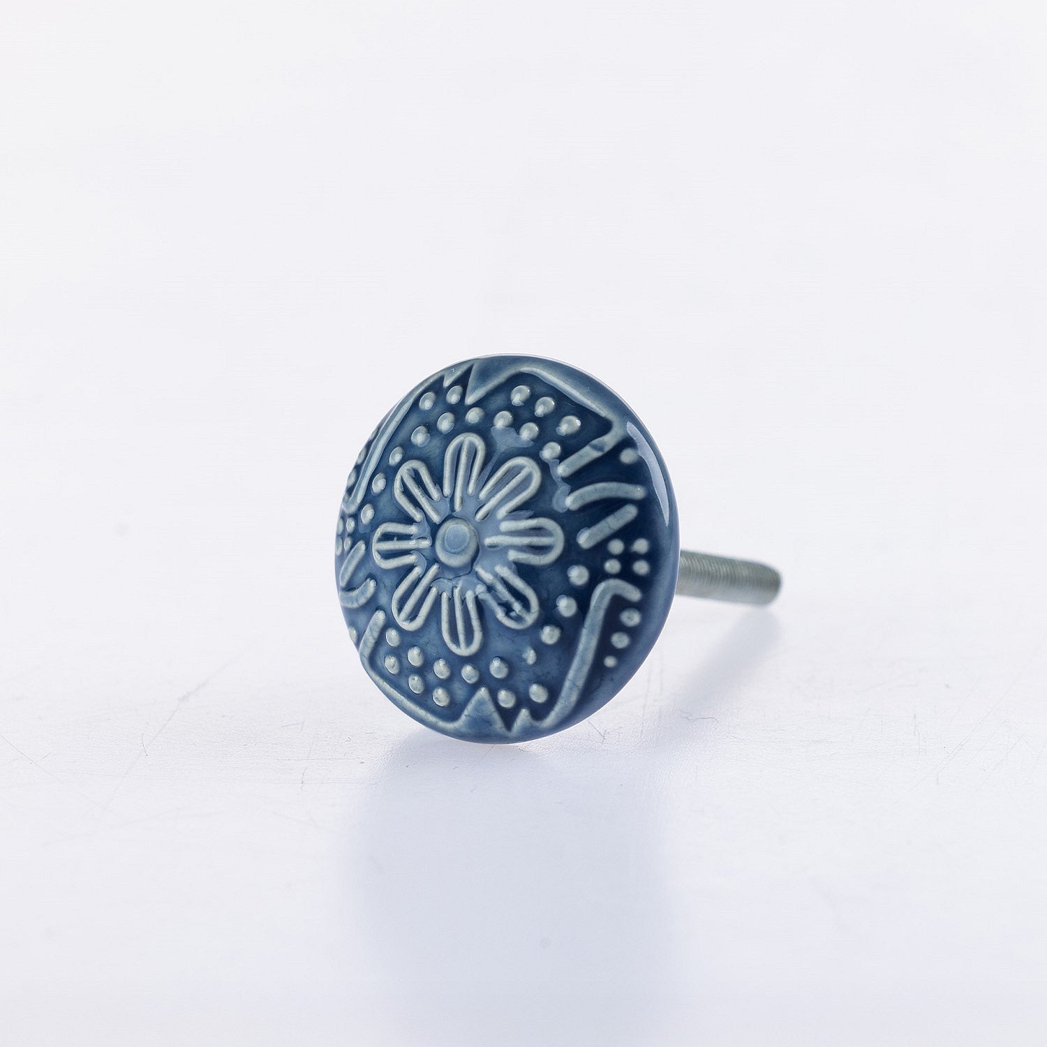 Denim ceramic round drawer knob with embossed floral pattern detailing and metal screw fitting.
