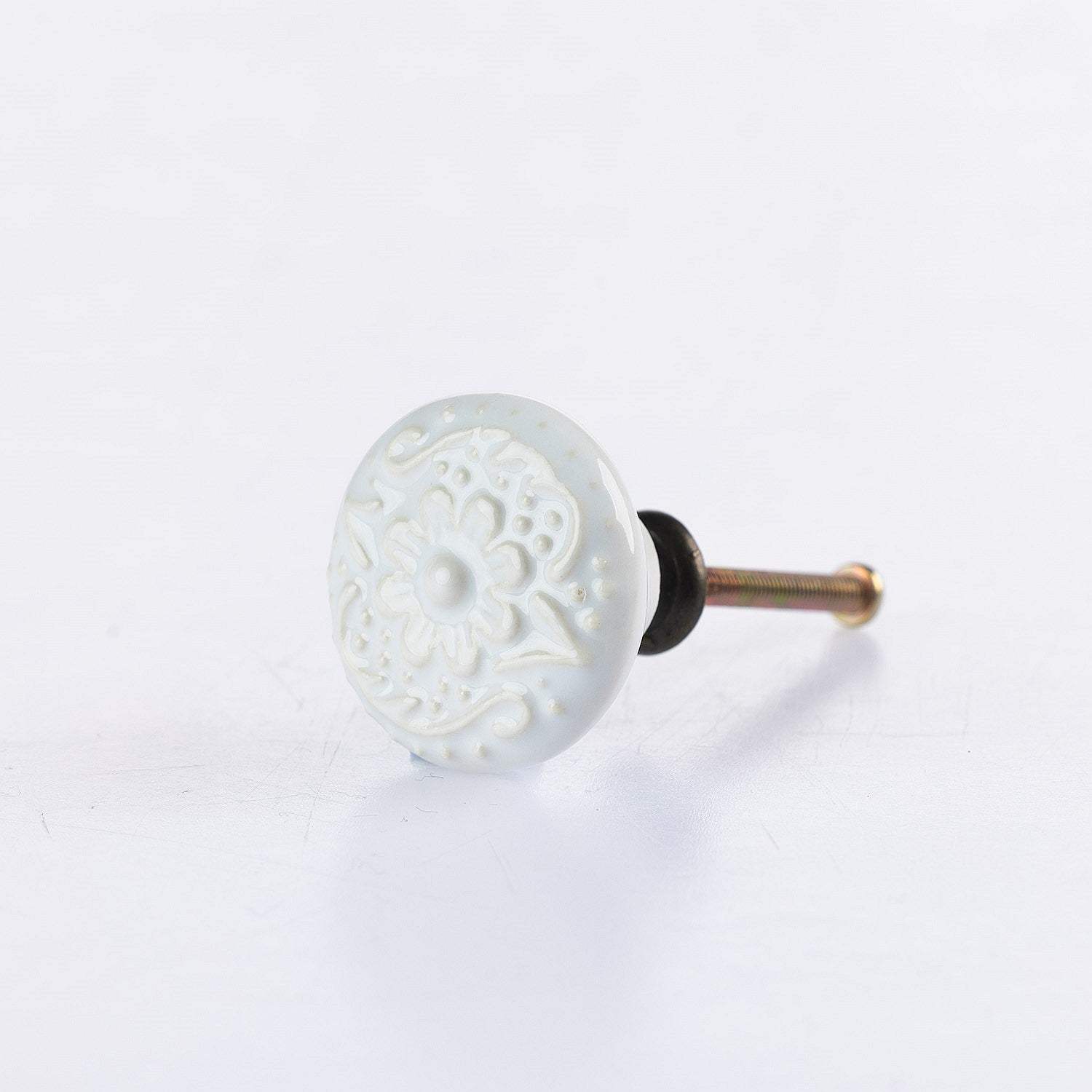 White ceramic round drawer knob with embossed floral pattern detailing and metal screw fitting.
