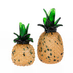 Small and large decorative glass pineapple ornaments with textured amber-coloured bodies and translucent green leaves displayed against a light grey background.