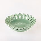 A small ceramic bowl with a scalloped, openwork edge and a glossy light green glaze, photographed on a plain white background.