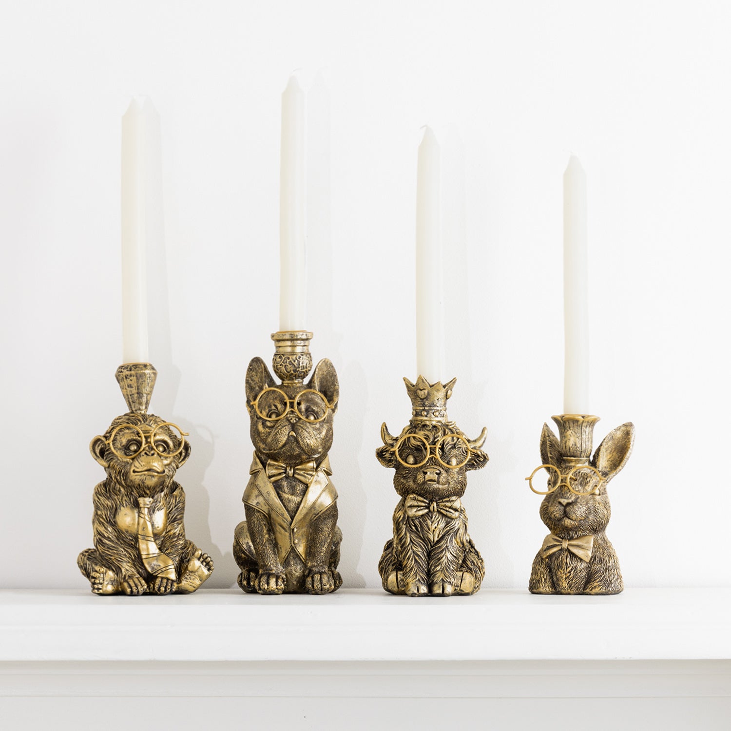 Four decorative animal candleholders with gold-tone glasses and white tapered candles on a white shelf.