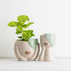 Abstract face planter with green plant and matching head vase on a white surface.