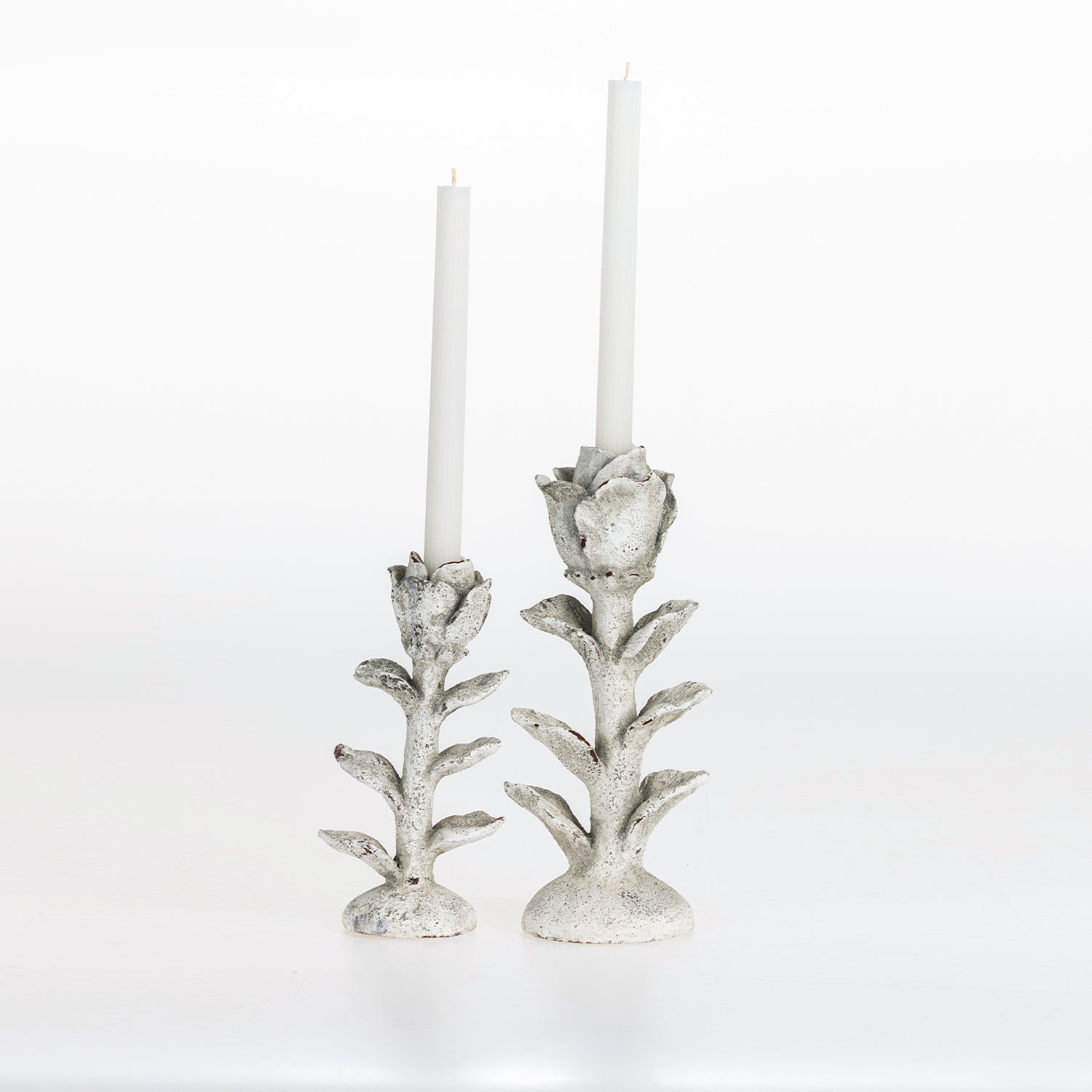 Small and large flower-shaped candle holders with white taper candles on a white background.