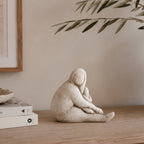 Cove Franco ceramic lady resting figurine displayed on a wooden console with stacked books and olive branches in a warm, neutral interior.