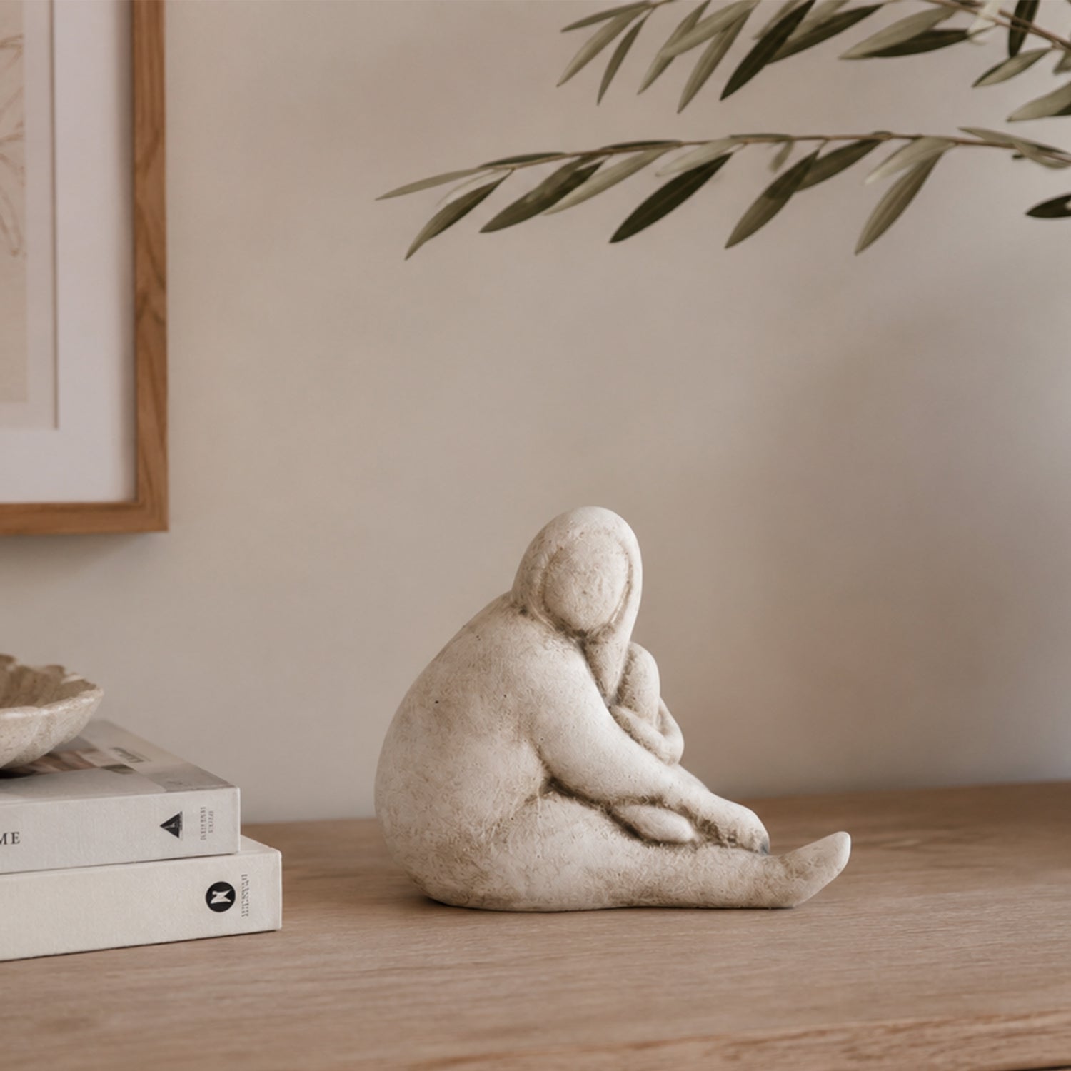 Cove Franco ceramic lady resting figurine displayed on a wooden console with stacked books and olive branches in a warm, neutral interior.