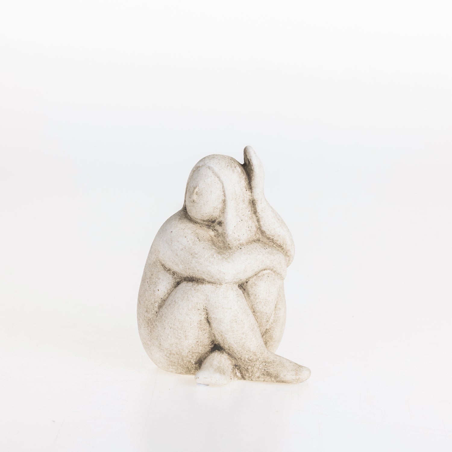 Abstract ceramic lady figurine in a natural stone-look finish seated in a contemplative pose on a white background.