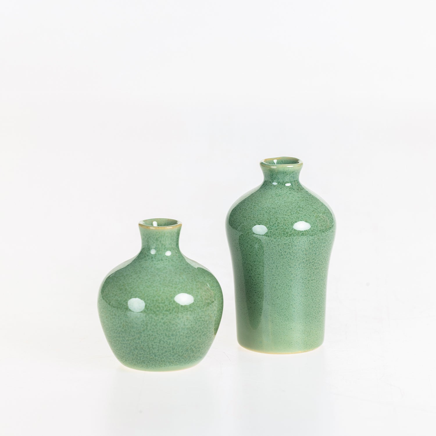 Two glossy green ceramic bud vases in rounded and bottle-shaped designs shown on a white background.