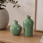 Two green ceramic bud vases displayed on a wooden console beside a textured stone-look vase with olive branches in a warm, contemporary interior.