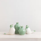 Two green ceramic bud vases with matching white and green decorative bird figurines displayed on a white shelf.