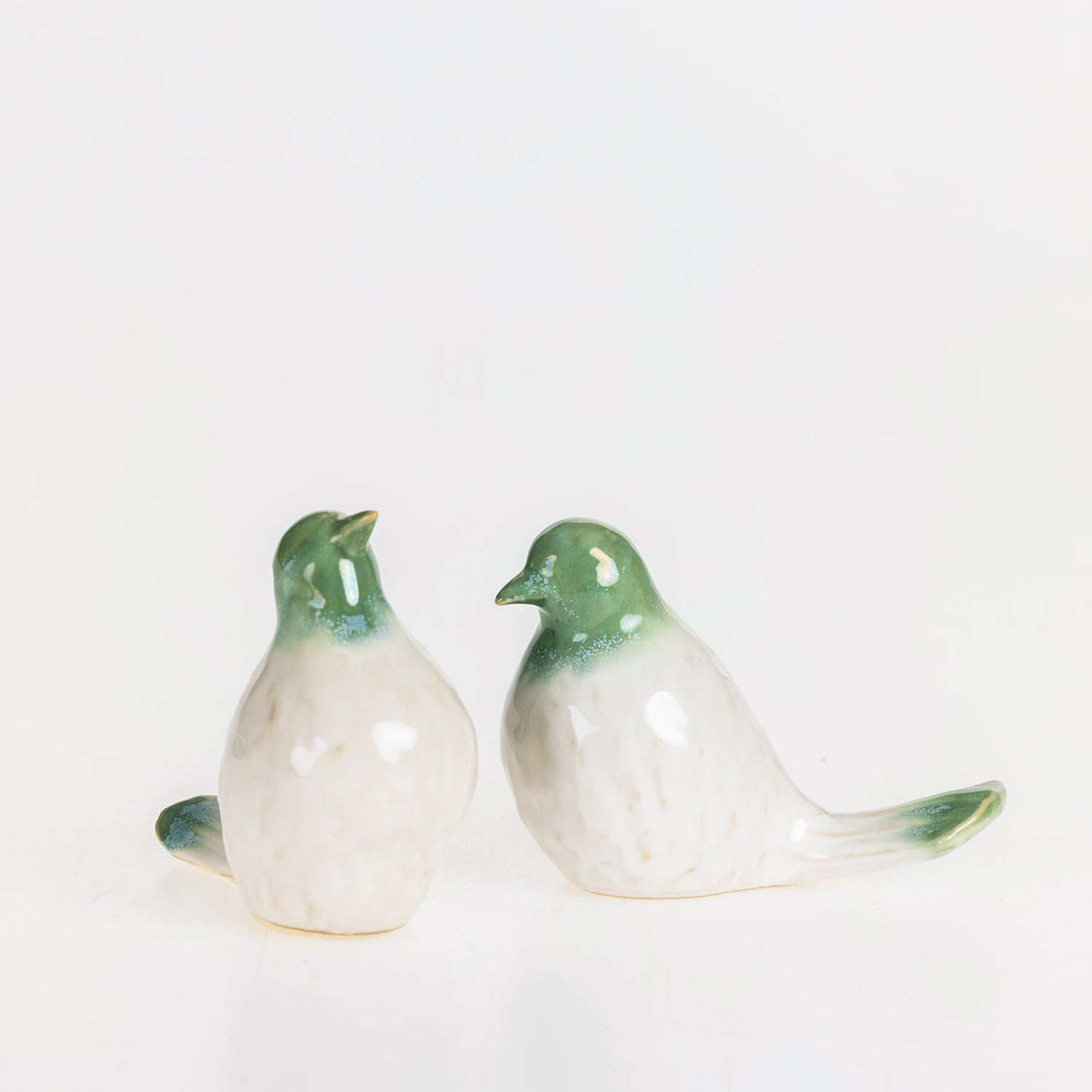 Two glossy ceramic bird figurines with green heads and tails and white bodies displayed together on a white background.