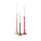 Three decorative candle holders in blush pink, green and fuchsia, each displayed with a white taper candle and arranged together against a white background.