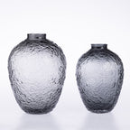 Two textured glass vases in different sizes, made of smoky transparent glass with a hammered surface, set against a clean white background.