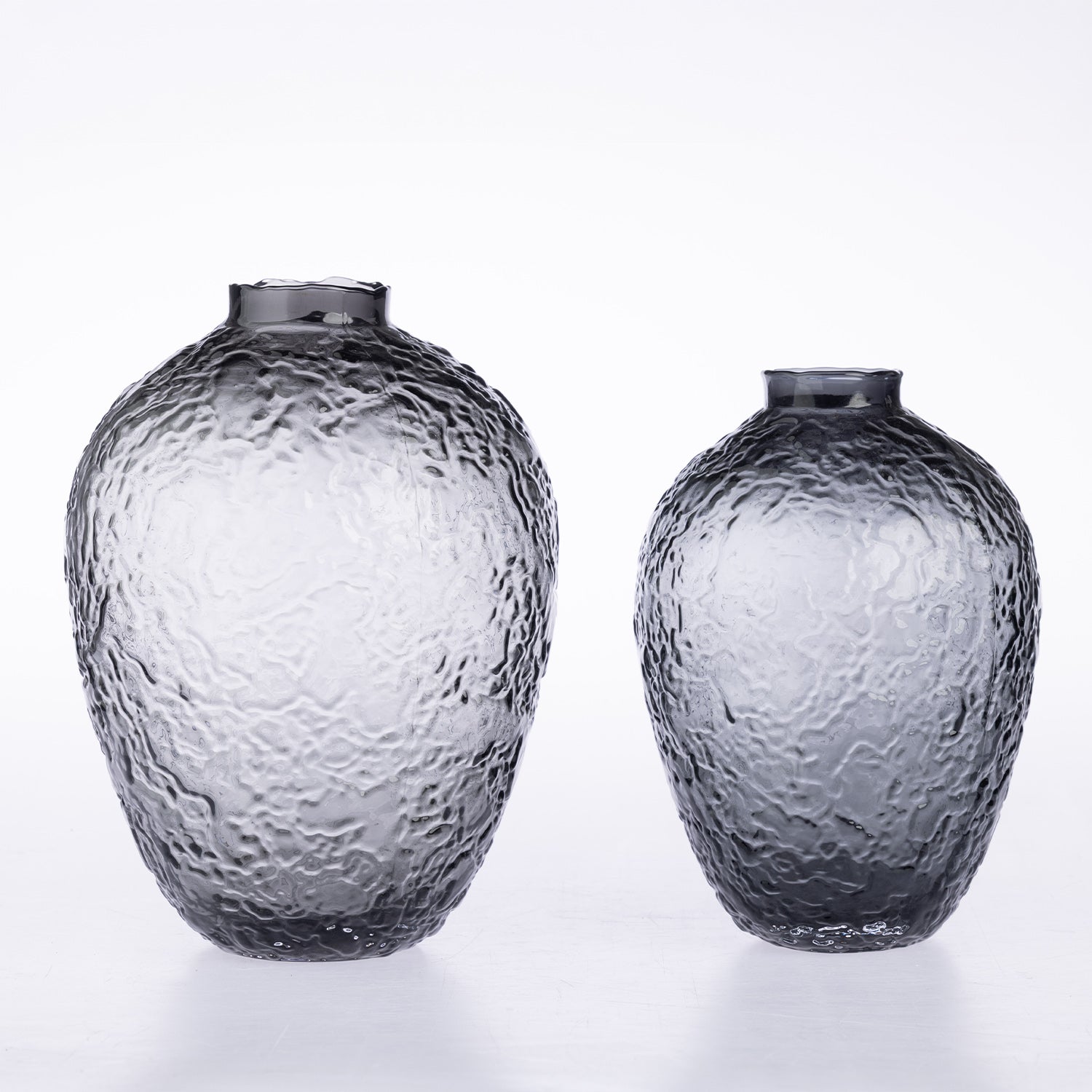 Two textured glass vases in different sizes, made of smoky transparent glass with a hammered surface, set against a clean white background.