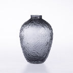 A textured dark gray glass vase with a short neck and rounded body, featuring a hammered or dimpled surface pattern, set against a plain white background.