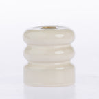A small round ceramic candle holder with a glossy, ribbed tiered design in a warm cream or off-white glaze, featuring a gold-toned metal wick insert at the top, set against a plain white background.