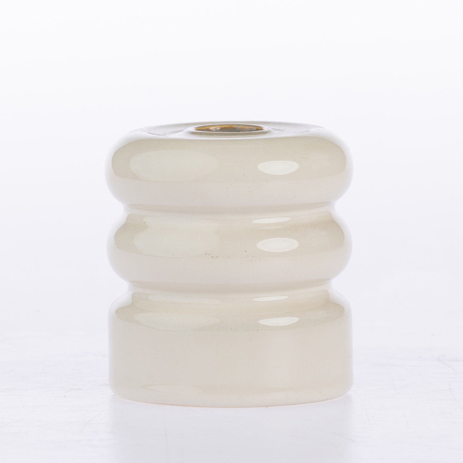 A small round ceramic candle holder with a glossy, ribbed tiered design in a warm cream or off-white glaze, featuring a gold-toned metal wick insert at the top, set against a plain white background.